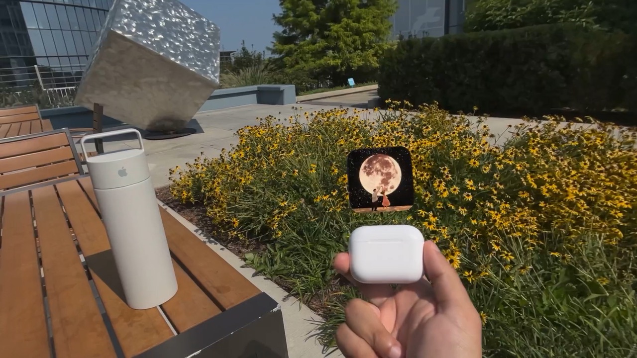 Album art floating above a closed AirPods case held in a hand